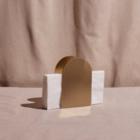 Gold arch-shaped napkin holder on a table against a beige background