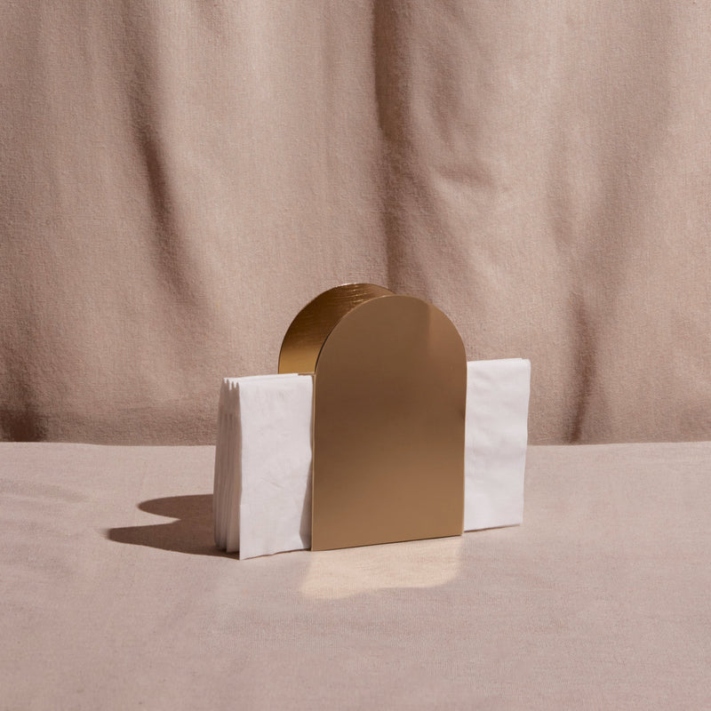 Gold arch-shaped napkin holder on a table against a beige background