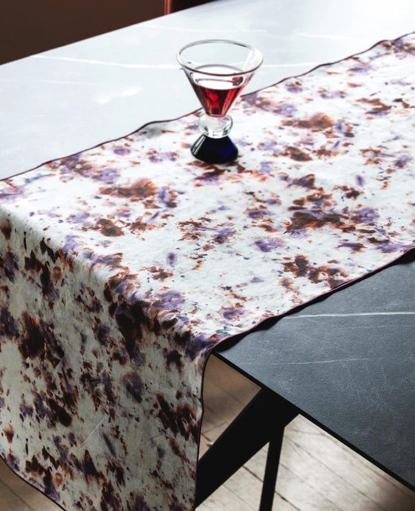 Marble patterned table runner on a table with a glass of red liquid.