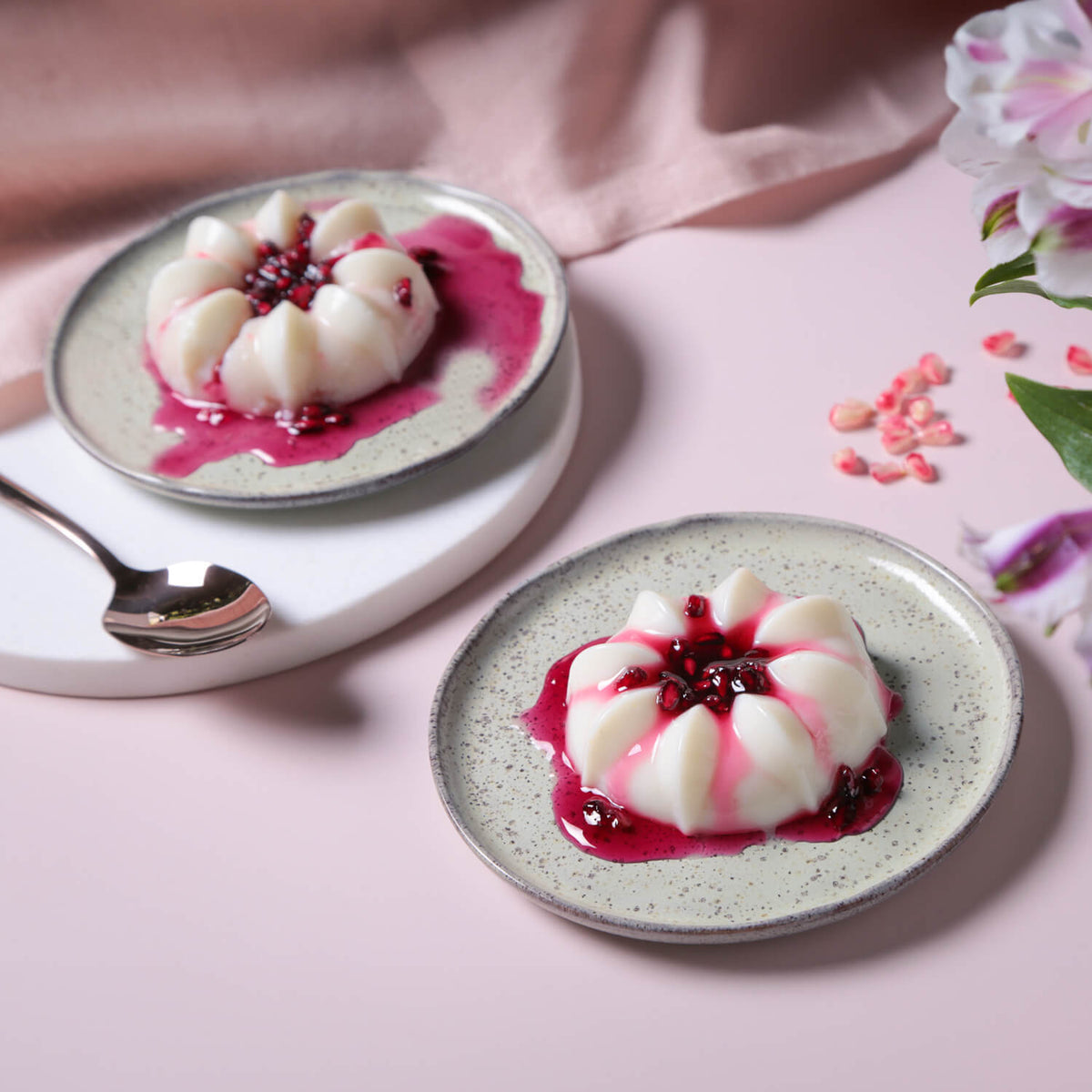 Two plates of dessert with pink sauce on a pink background