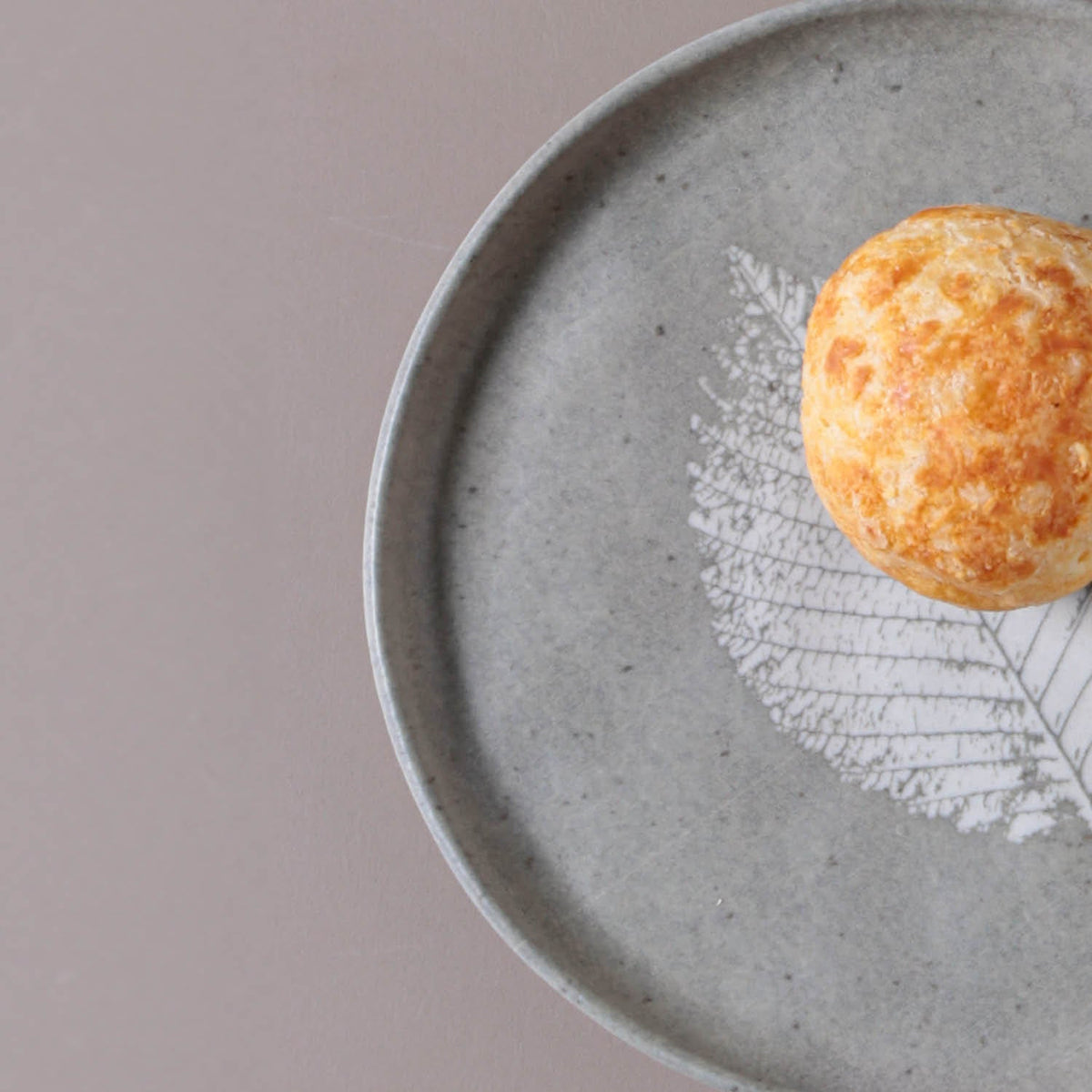 Round pastry on a gray ceramic plate with a leaf design on a beige background