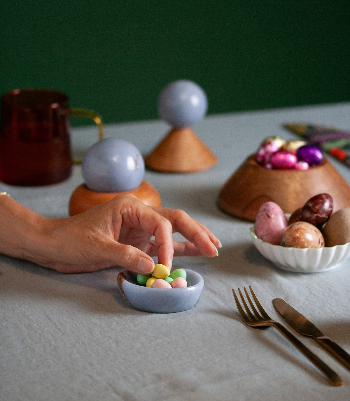 hand picking candy from a small blue stone dish on a table surface with other bowls holding candy and decorative objects