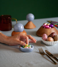 hand picking candy from a small blue stone dish on a table surface with other bowls holding candy and decorative objects