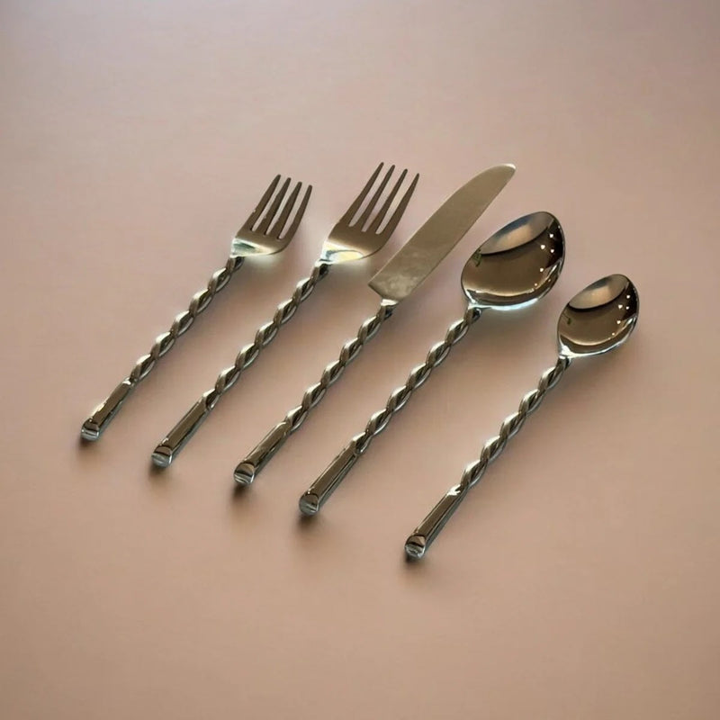 Set of silver cutlery including forks, a knife, and spoons on a pink background