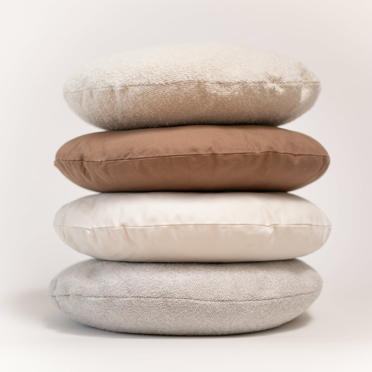 Stack of four round cushions in beige, brown, and gray on a white background