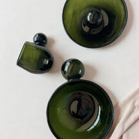 Three green glass containers on a light pink background