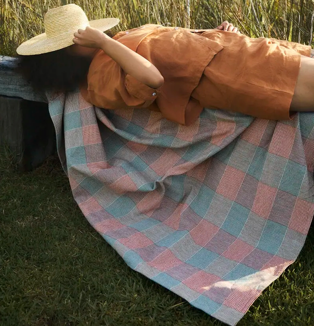 Person lying on a checkered blanket in a grassy field
