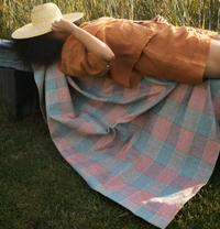 Person lying on a checkered blanket in a grassy field
