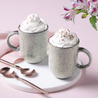 Two mugs with whipped cream on a pink background