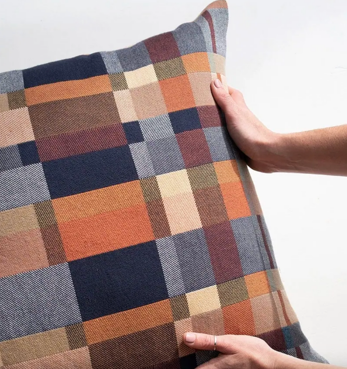 Plaid pillow with a hand holding it against a white background