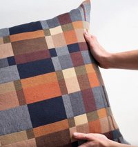 Plaid pillow with a hand holding it against a white background