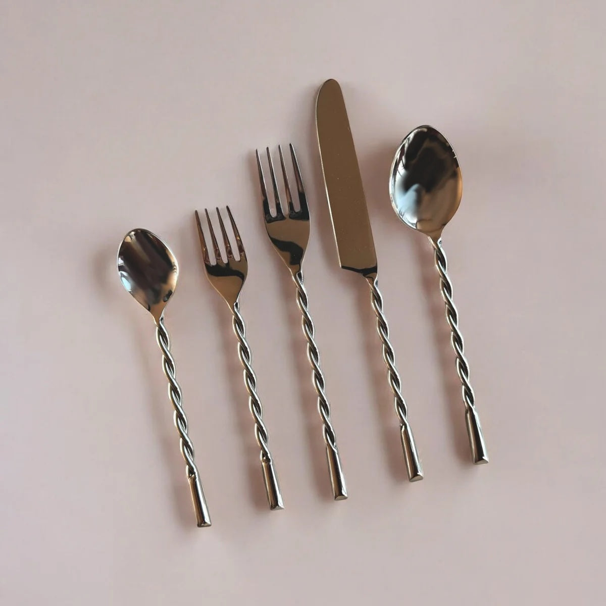 Set of silver cutlery with twisted handles on a light pink background