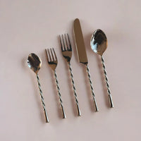 Set of silver cutlery with twisted handles on a light pink background