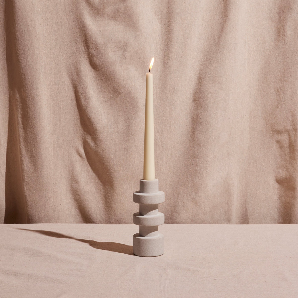 Candle in a decorative holder against a beige fabric background