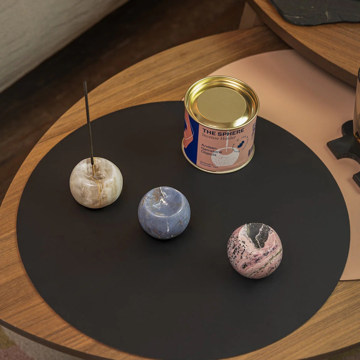Three marbled stone incense holders on a black mat with a can labeled 'The Sphere' on a wooden surface.