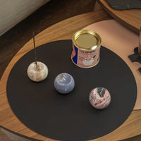 Three marbled stone incense holders on a black mat with a can labeled 'The Sphere' on a wooden surface.