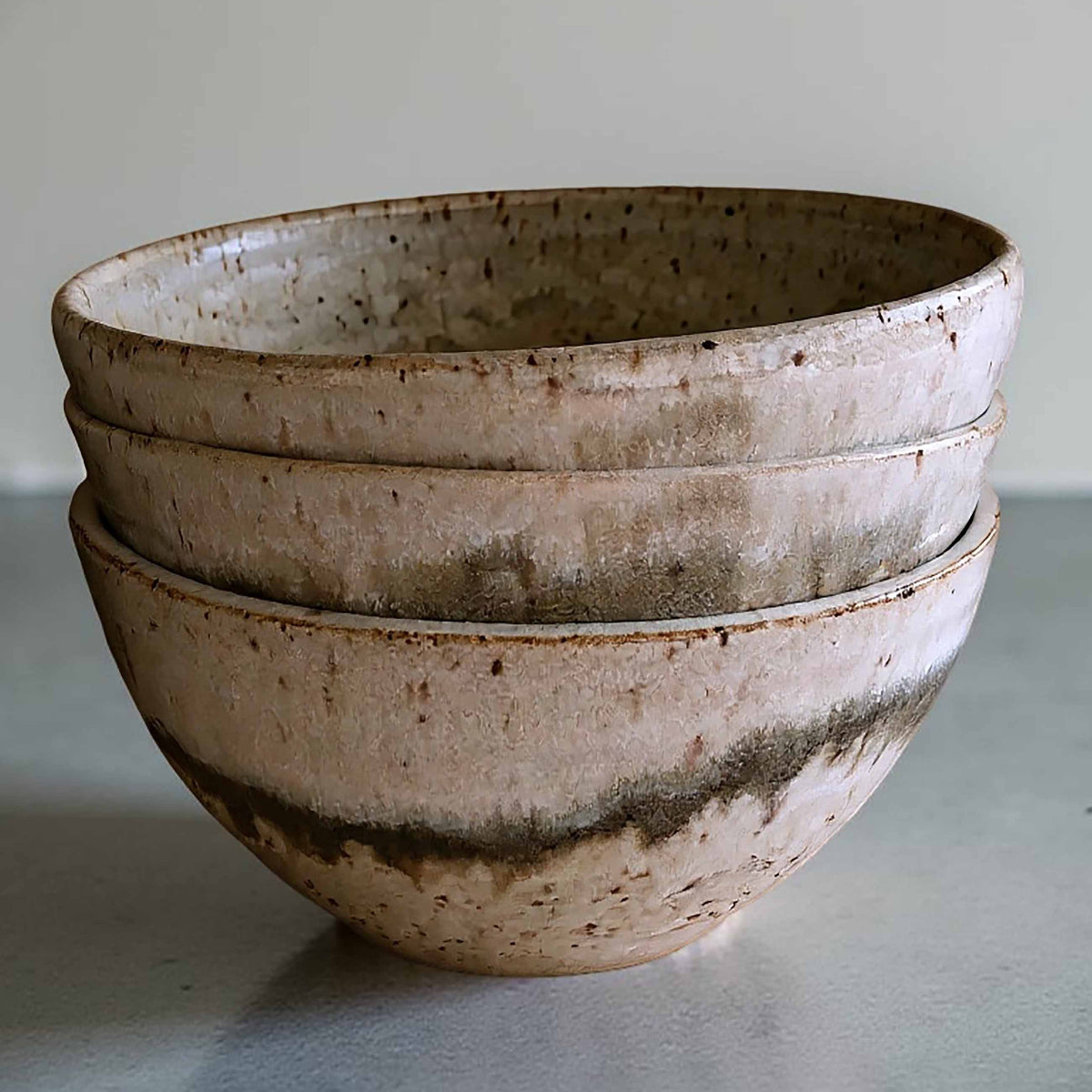 Ceramic bowl with light and dark neutral glaze details on a grey surface