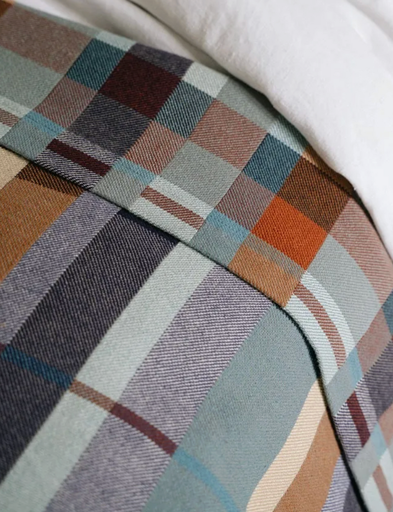 A close-up of a plaid fabric textile with a muted multicolor pattern, draped over a white surface.
