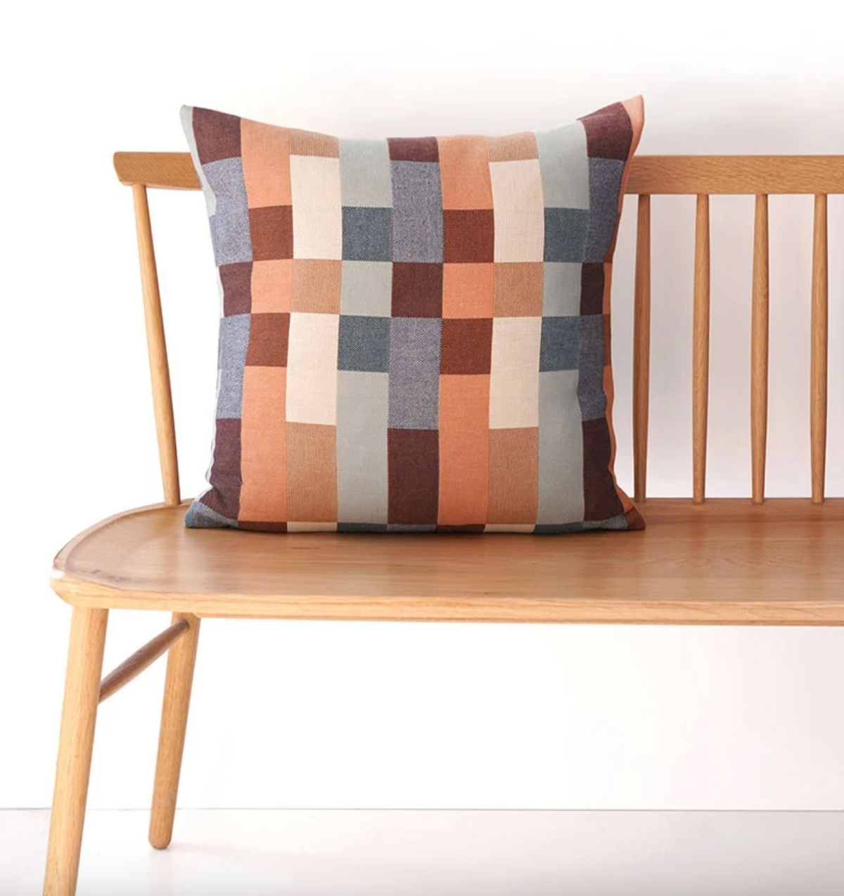 Colorful geometric-patterned pillow on a wooden bench against a white background