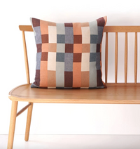 Colorful geometric-patterned pillow on a wooden bench against a white background