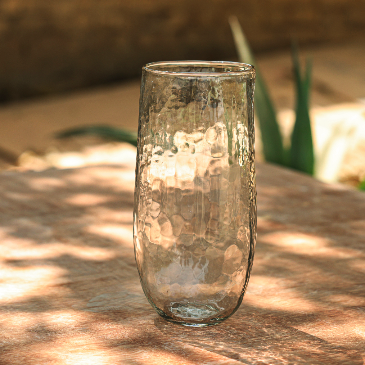 Clear glass vase on a wooden surface with natural light and greenery in the background