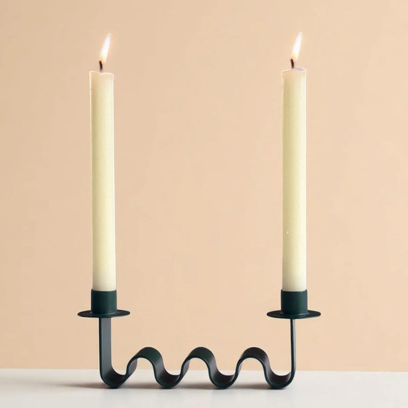 Wavy green candle holder with two lit candles on a beige background