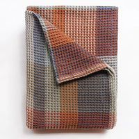 Folded woven blanket with a checkered pattern on a white background