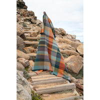 A multicolor plaid blanket or throw draped over a wooden pathway on a rocky outdoor hillside.