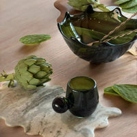 Green glass bowl and cup with artichoke and leaves on a wooden surface