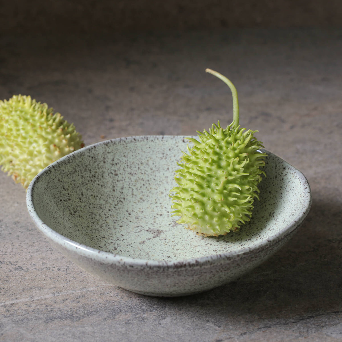 Green fruit in a ceramic bowl on a stone surface