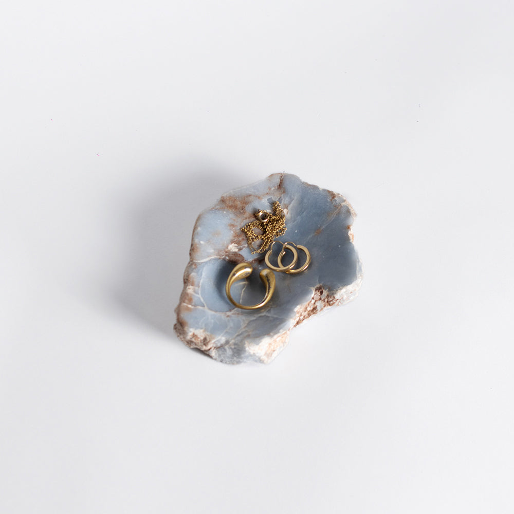 Gold jewelry in a decorative stone dish with a light gray background