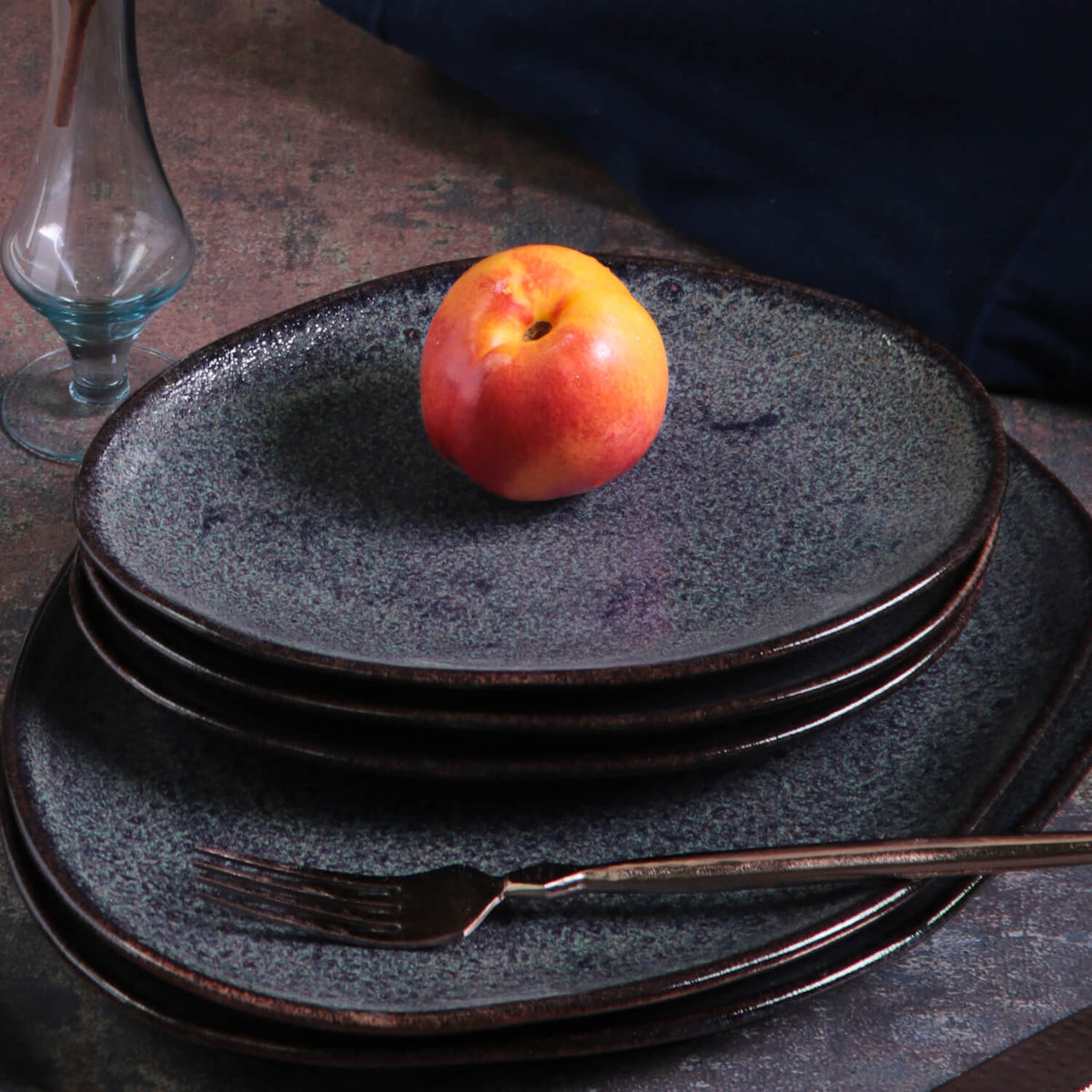 Set of dark ceramic plates with a single apple on top, placed on a textured surface.