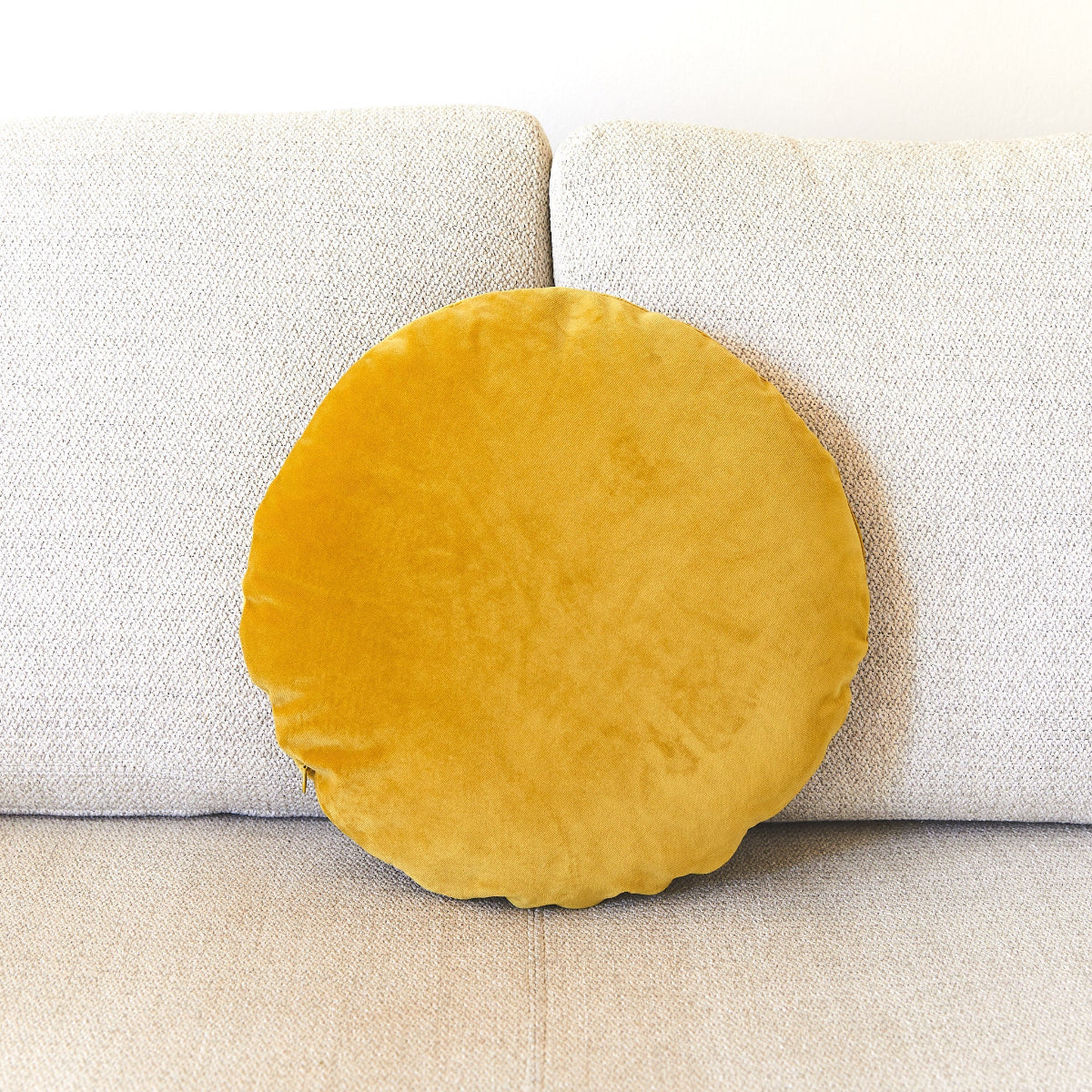 Round mustard yellow pillow on a beige sofa