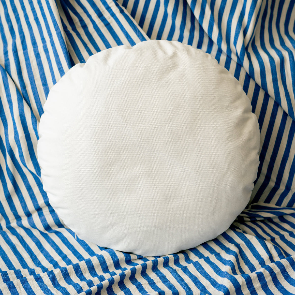 Round white pillow on a blue and white striped fabric background
