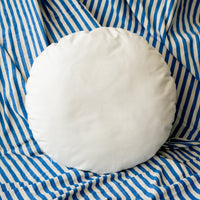 Round white pillow on a blue and white striped fabric background
