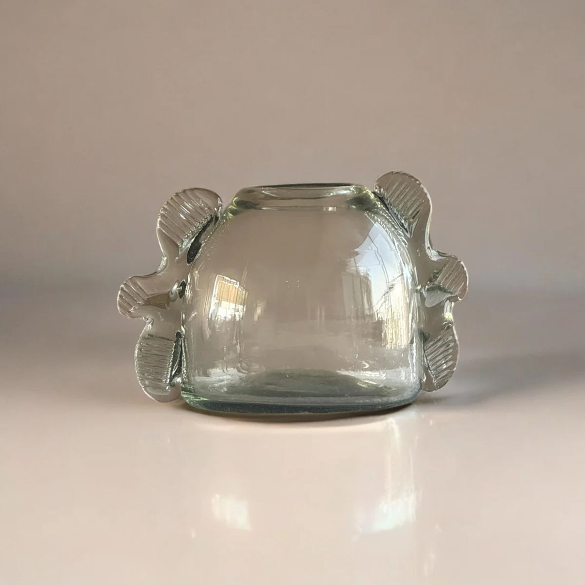 Clear glass bud vase with textured handles on a reflective surface