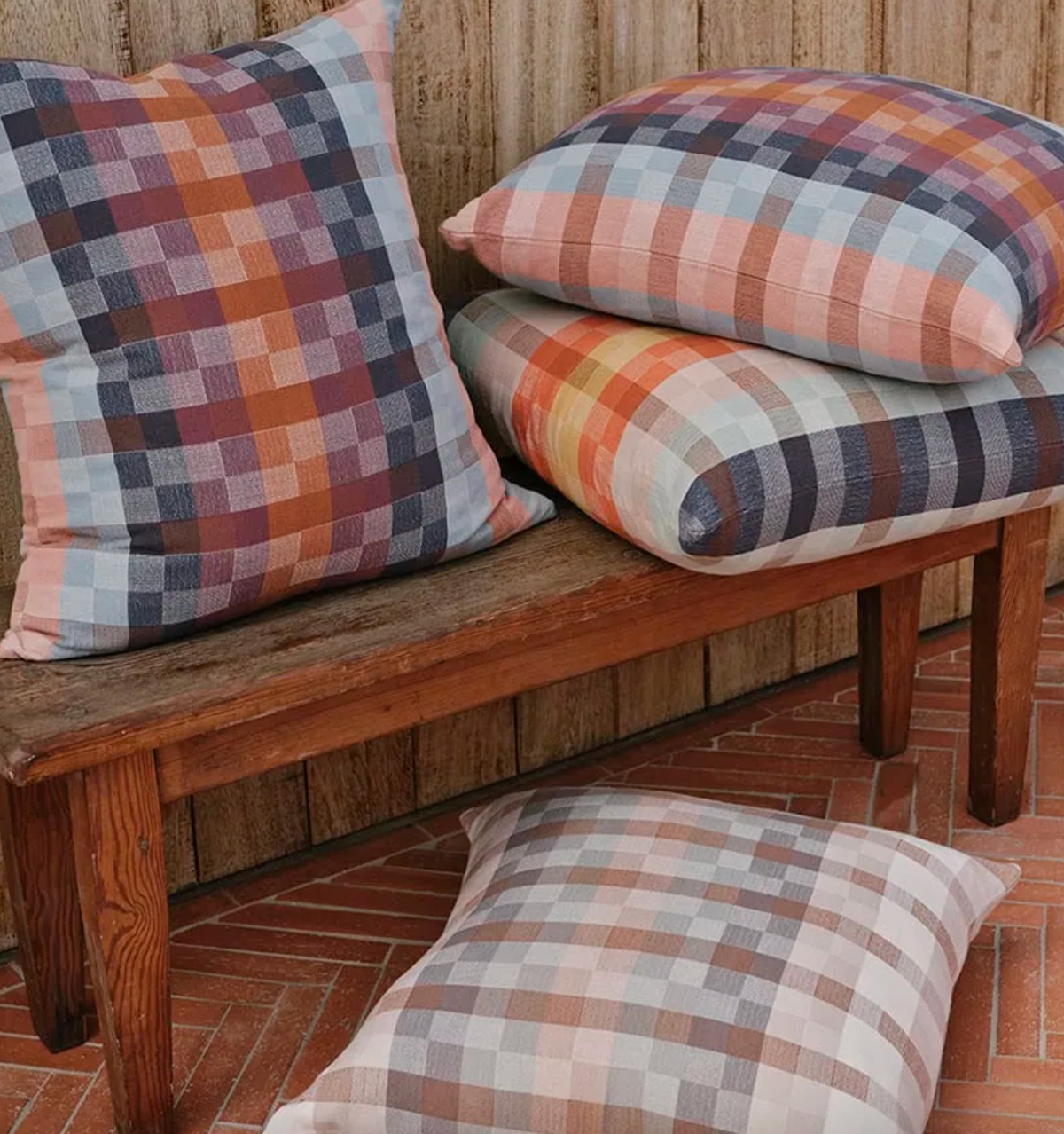 Plaid cushions on a wooden bench against a wooden wall.