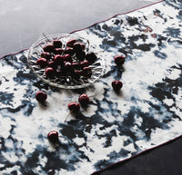 Cherries on a glass plate and scattered on a marble table runner