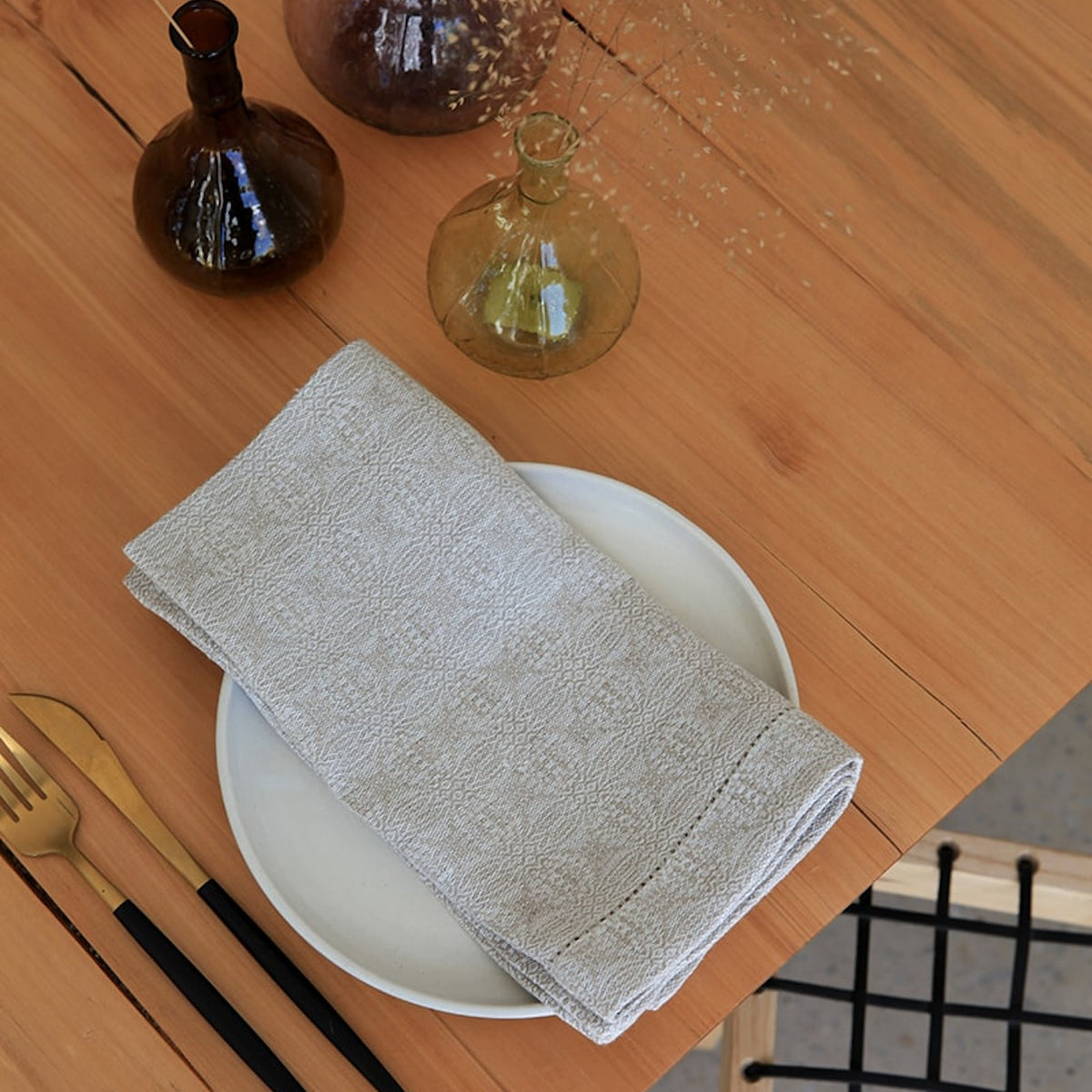 Folded natural napkin on a white plate with a wooden table and decorative bottles in the background.