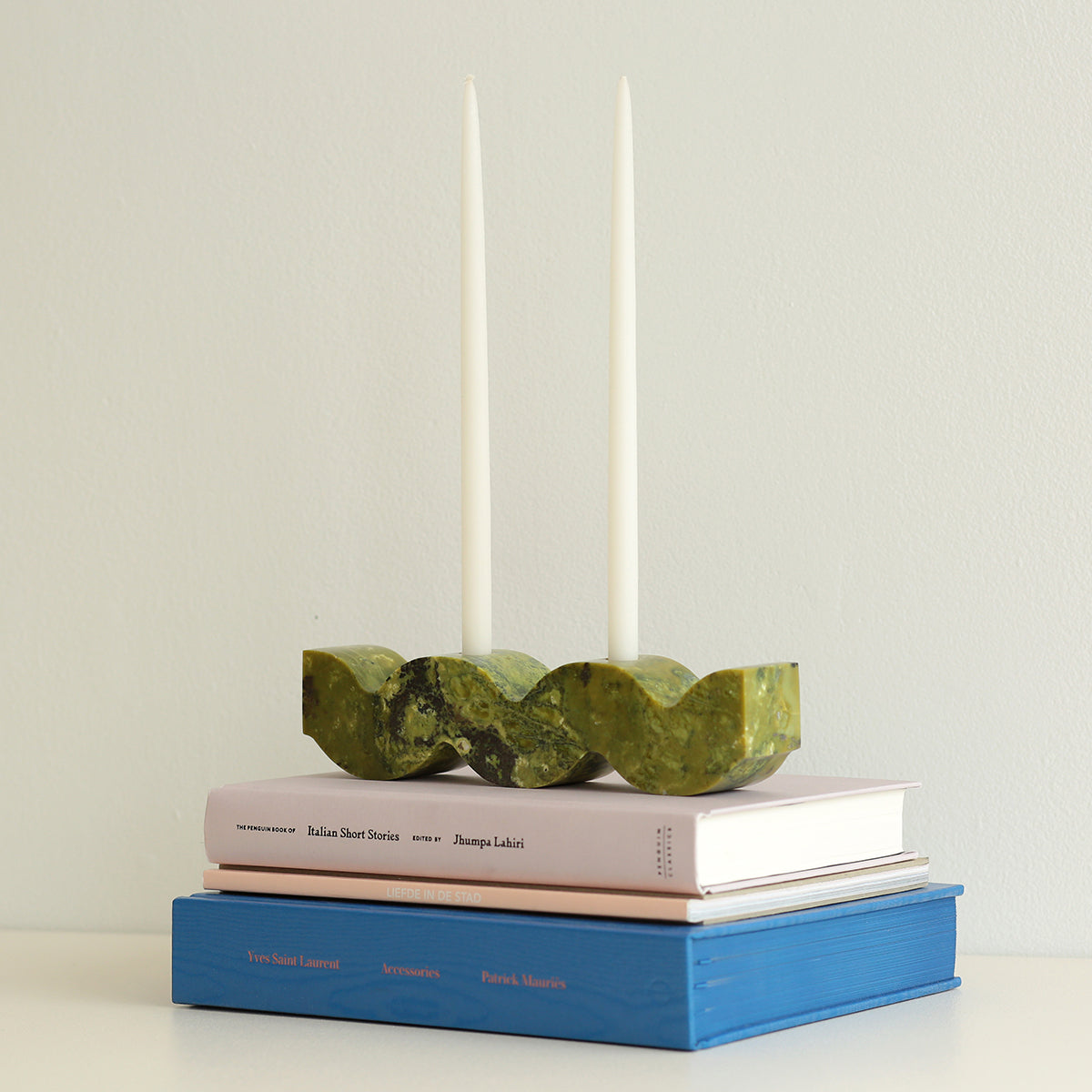 Green wavy stone candle holder on top of books with two taper candles in the background