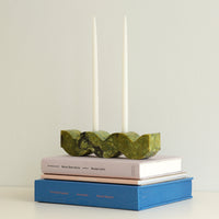 Green wavy stone candle holder on top of books with two taper candles in the background