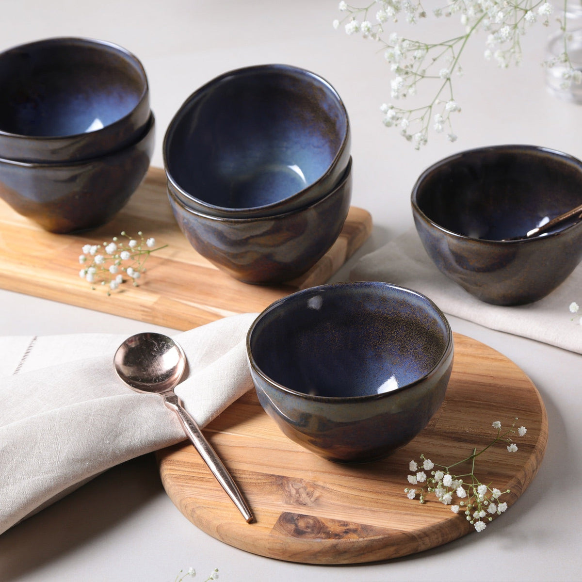 Set of dark blue ceramic bowls on a wooden tray with a spoon and white flowers.
