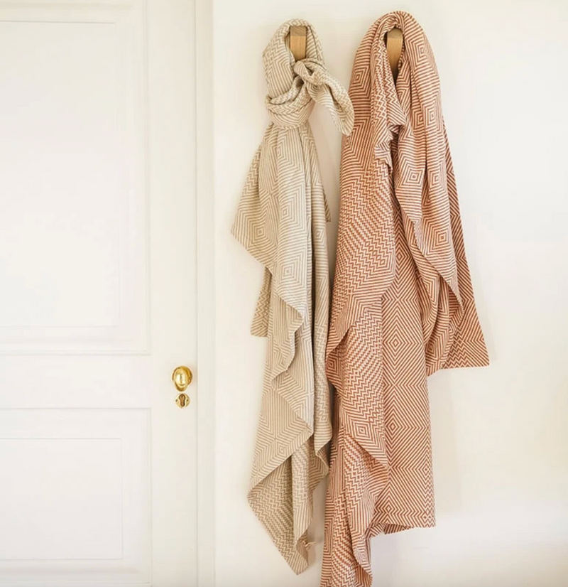 Two blankets hanging on wall hooks next to a door with a gold doorknob.