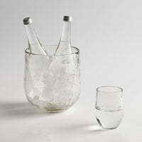 Glass ice bucket filled with two bottles and a drinking glass of water on a white background