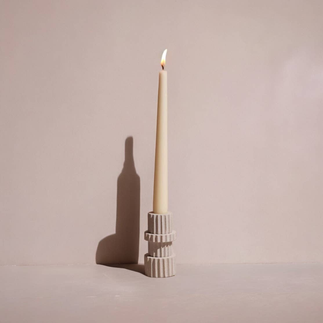 Sandstone taper candle holder with a lit candle on a plain background