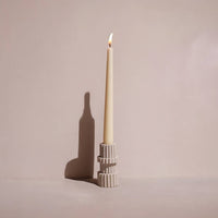 Sandstone taper candle holder with a lit candle on a plain background
