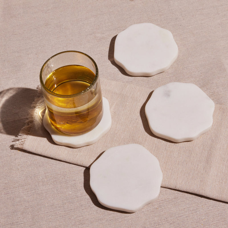 Glass of amber liquid on hexagonal marble coasters on a beige surface