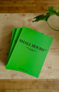 Green magazine titled 'Small Hours' on a wooden surface with a plant leaf.