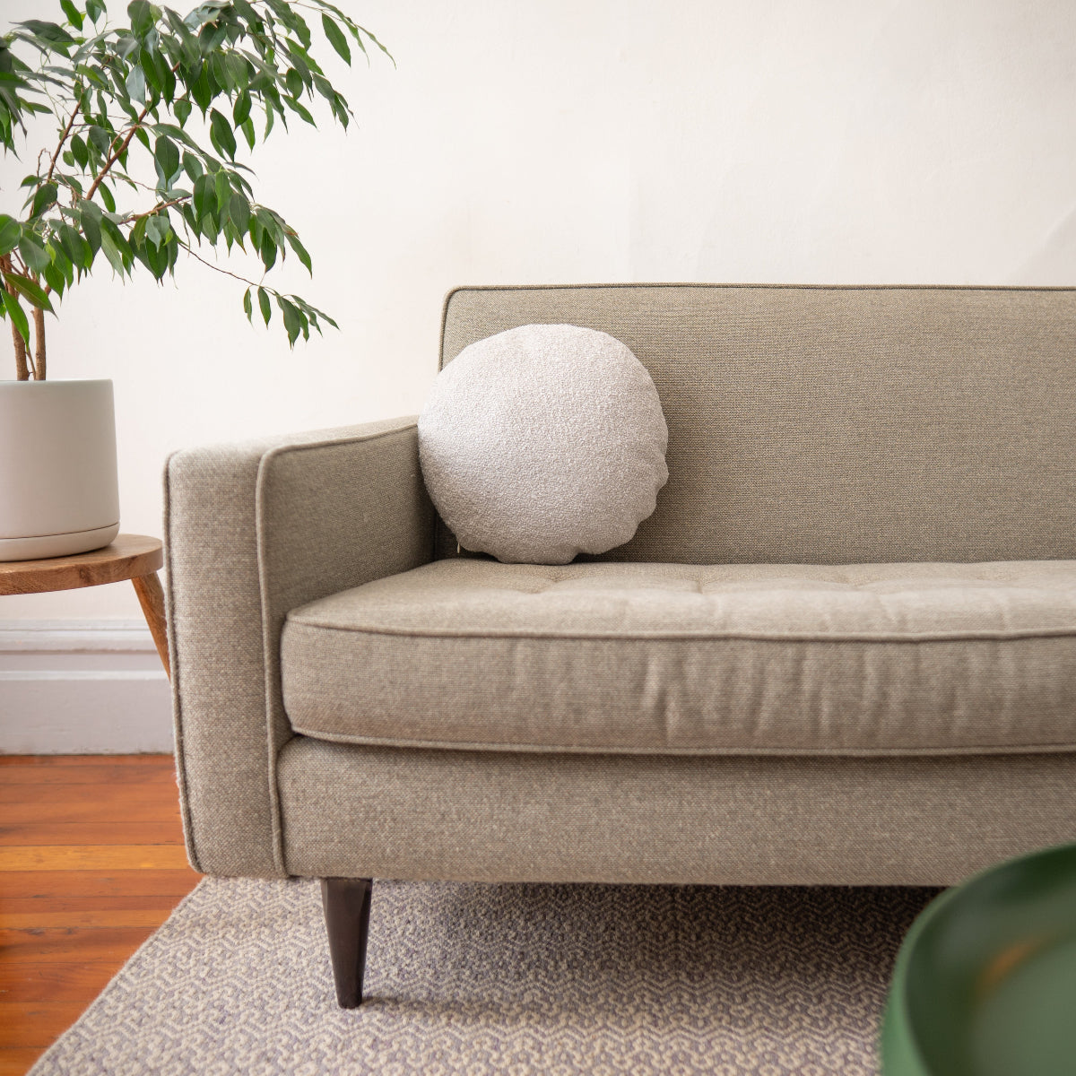 Beige sofa with a round light grey pillow in a living room setting