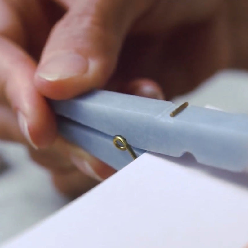 Close-up of hands using a stone clothespin on a white surface